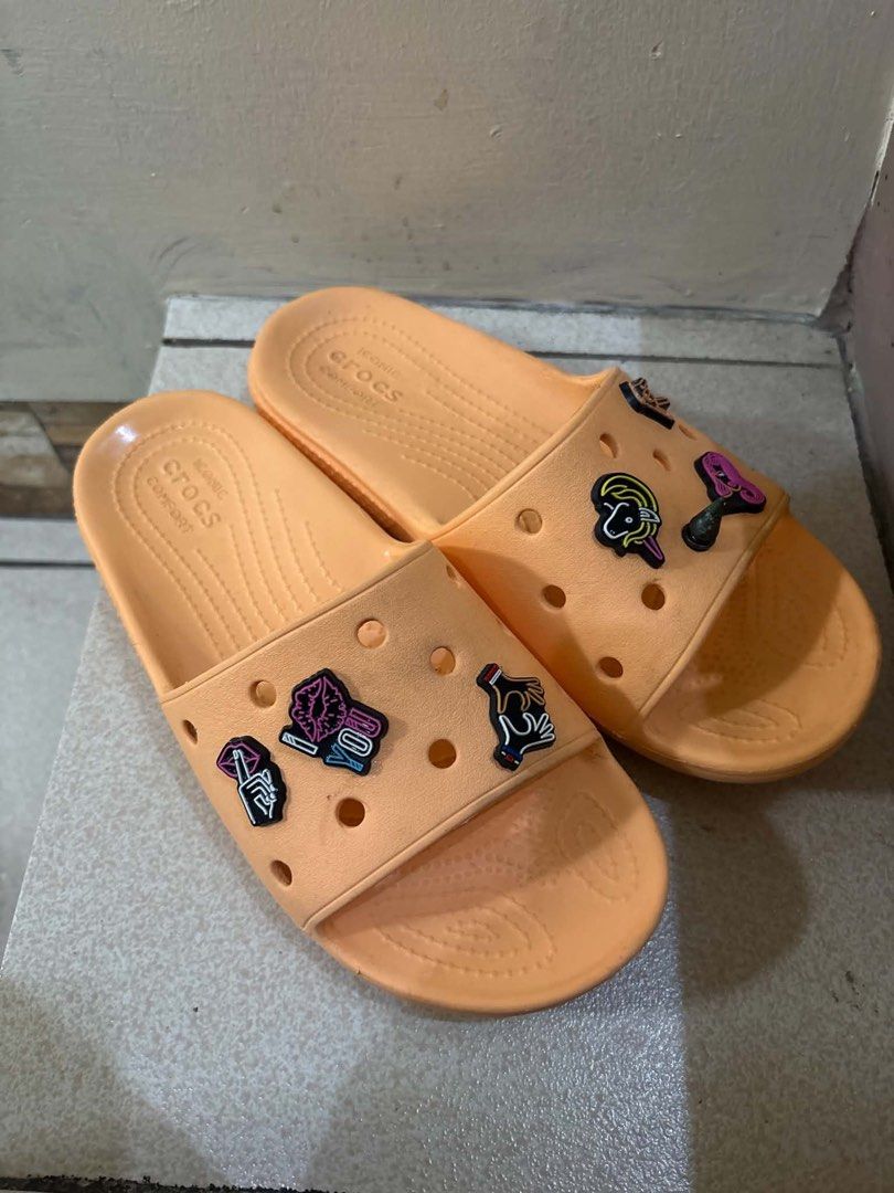 Crocs Orange Slides with Jibbitz Charms (Category: Slippers and slides) located in San Juan City. Submitted by kimtiongson (Listing ID 1469956872, Image 1). Description: - Color: Bright orange - Style: Classic comfort slip-on slides - Customization: Fun Jibbitz charms already attached to the straps - Condition: Light wear on the footbeds, sole grips still clean and intact - Ideal for: Indoor lounging or casual outdoor errands.