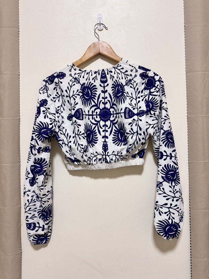 Crop Top Long Sleeve (Category: Sleeveless) located in Manila. Submitted by seayouncey (Listing ID 1470057134, Image 2). Description: - Style: White crop top with dark blue floral print - Neckline: V-neck wrap front with grid stripe trim - Sleeves: Long sleeves with elastic cuffs - Fit: Comfortable elastic waistband, lightweight fabric - Back: Matching all-over floral pattern - Pairing: Great with high-waisted jeans or skirts.
