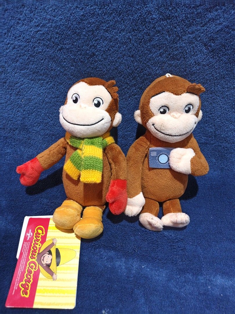 Curious George Plush Toys Set with Tag (Category: Plushies & Soft Toys) located in Manila. Submitted by kirstentoyshub (Listing ID 1470016297, Image 1). Description: - Set of 2 adorable Curious George plush toys - First plush: Wears a green/yellow striped scarf, red mittens, and yellow boots; includes original paper tag - Second plush: Features a small blue camera accessory and a hanging loop on top - Made with ultra-soft brown plush material and