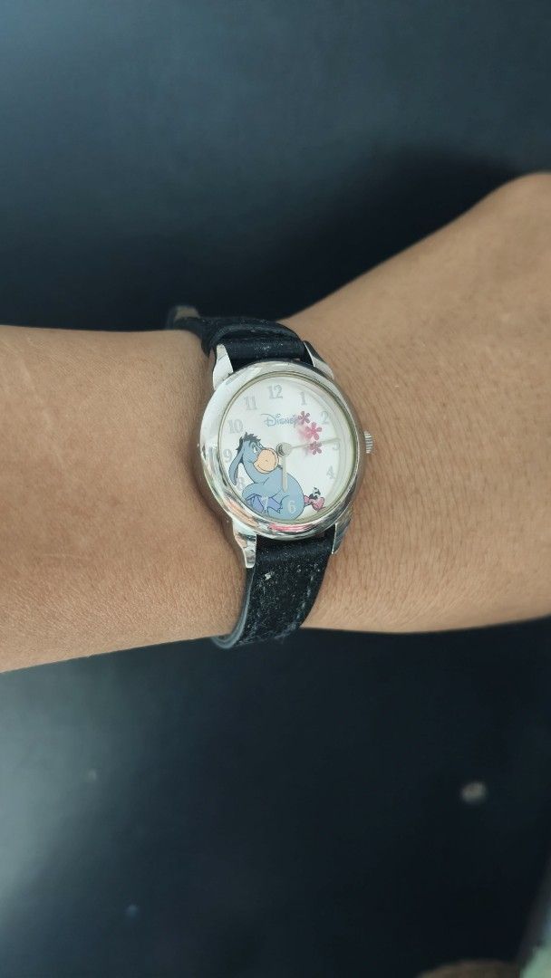 Disney Eeyore analog wrist watch with black strap (Category: Women's Watches) located in Taguig. Submitted by mercyeugen28914 (Listing ID 1470097940, Image 2). Description: - Authentic Disney analog watch featuring an adorable Eeyore graphic - Lovely pink floral design on a clean white dial - Classic silver-tone case with standard number hour markers - Comfortable black leather-like strap with a secure silver buckle - Fun and collectible piece, p