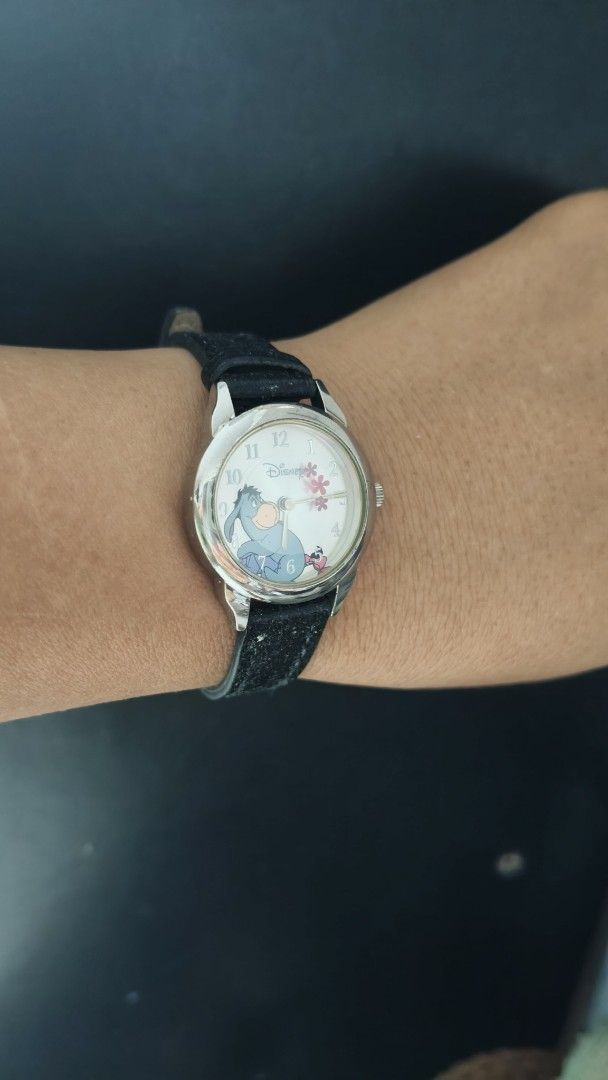 Disney Eeyore analog wrist watch with black strap (Category: Women's Watches) located in Taguig. Submitted by mercyeugen28914 (Listing ID 1470097940, Image 3). Description: - Authentic Disney analog watch featuring an adorable Eeyore graphic - Lovely pink floral design on a clean white dial - Classic silver-tone case with standard number hour markers - Comfortable black leather-like strap with a secure silver buckle - Fun and collectible piece, p