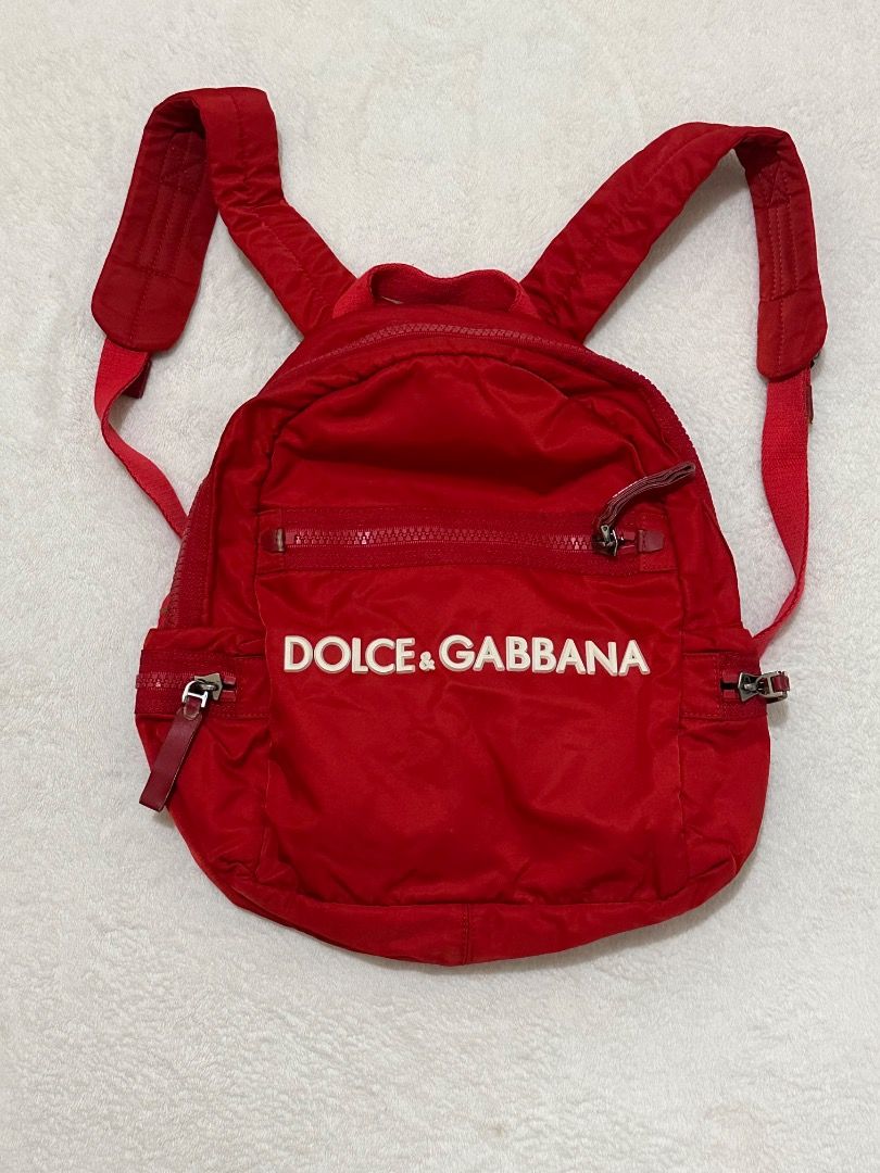 Dolce & Gabbana Red Nylon Mini Backpack (Category: Babies & Kids Fashion) located in Adams. Submitted by ni-collection26 (Listing ID 1470035134, Image 1). Description: - Brand: Dolce & Gabbana red bag AUTHENTIC - Material: Durable bright red nylon with matching interior lining - Design: Big bold white logo stamped on the front pocket - Storage: Top zip closure, front zip pocket, side zip pockets, and a back slip-in card window pocket - Straps: Ad