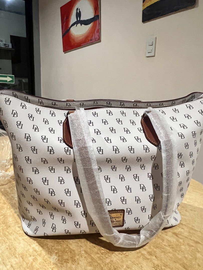 Dooney & Bourke DB Monogram Tote Bag (Category: Tote Bags) located in Davao. Submitted by sammmdizon7 (Listing ID 1470066200, Image 3). Description: - Authentic Dooney & Bourke tote bag - Iconic white & dark brown DB monogram print - Gold-tone hardware with front logo patch - Bright red interior lining with zip and slip pockets - Secure top zip closure - Brand new: handles still wrapped in original protective packaging - Includes original product