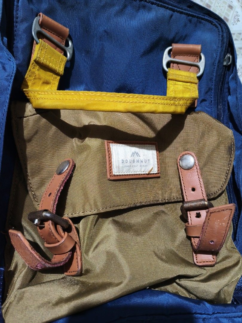 Doughnut Blue and Brown Backpack with Yellow Handle (Category: Backpacks) located in Quezon City. Submitted by affordable1 (Listing ID 1470059858, Image 1). Description: - Brand: Doughnut - Colorway: Blue, brown, and yellow - Material: Durable nylon body with leather buckle straps and metal hardware - Closure & Straps: Zipper top closure with adjustable shoulder straps and metal sliders - Condition: Pre-loved with some tarnishing and rust spots o