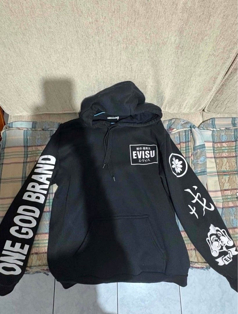 Evisu Black Hoodie (Category: Coats, Jackets and Outerwear) located in Manila. Submitted by jaysieseva620 (Listing ID 1470075773, Image 1). Description: - Brand: Evisu - Color: Black with contrasting white graphics - Material: Premium heavy cotton - Front: Text box logo and functional pouch pocket - Sleeves: 'ONE GOD BRAND' on the right, Japanese character and deity graphic on the left - Back: Large signature white gull logo with registered trade
