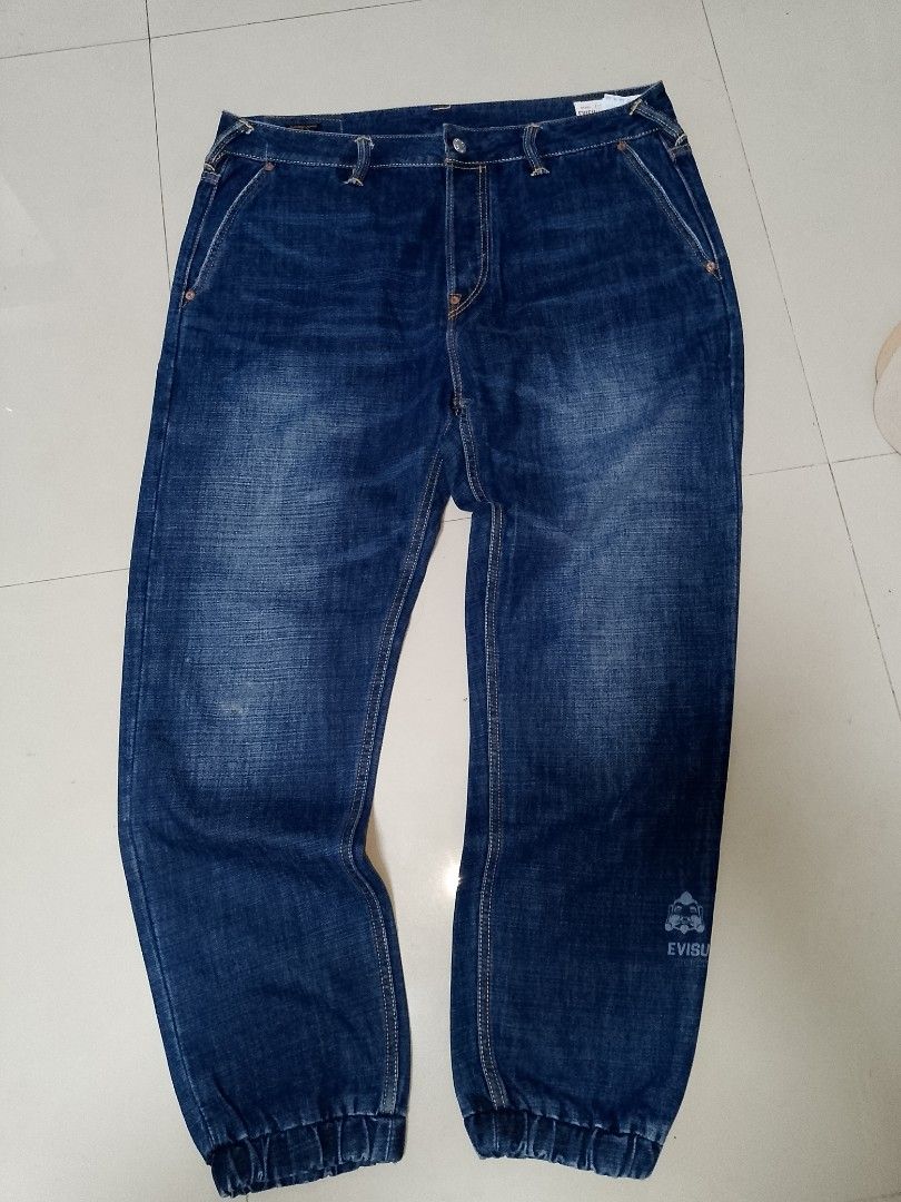 Evisu Daruma Camo Denim Joggers Size 36 (Category: Jeans) located in Manila. Submitted by mjthrifted_second (Listing ID 1469987803, Image 2). Description: - Brand: Evisu Daruma - Size: 36 (marked on leather patch) -Actual Size: 37/41 - Color/Wash: Clean blue denim - Unique Design: Camo print panels down the back and Daruma character graphics near the lower leg - Details: Elasticated ankle cuffs, button fly closure, and classic contrast stitching 