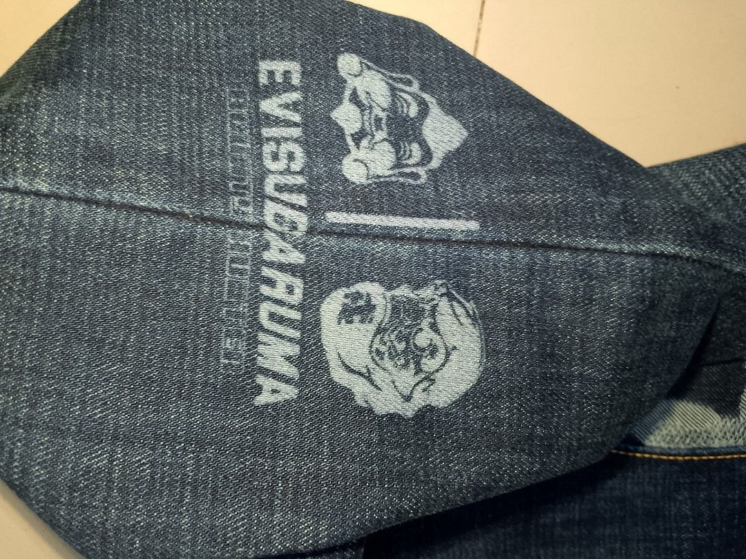 Evisu Daruma Camo Denim Joggers Size 36 (Category: Jeans) located in Manila. Submitted by mjthrifted_second (Listing ID 1469987803, Image 3). Description: - Brand: Evisu Daruma - Size: 36 (marked on leather patch) -Actual Size: 37/41 - Color/Wash: Clean blue denim - Unique Design: Camo print panels down the back and Daruma character graphics near the lower leg - Details: Elasticated ankle cuffs, button fly closure, and classic contrast stitching 