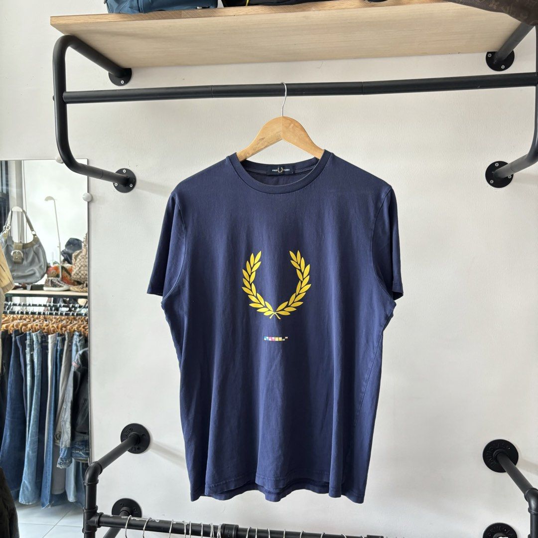 Fred Perry Navy Blue T-Shirt Size L (Category: Tshirts & Polo Shirts ) located in Bambang. Submitted by heats777 (Listing ID 1470018798, Image 2). Description: - Brand: Fred Perry - Style: Casual knit t-shirt / crew neck - Color: Navy blue - Size: Large (L) - Material: 100% cotton (comfortable for daily wear) - Design: Large yellow laurel wreath logo with multi-color graphic block detail on the chest - Origin: Made in China.