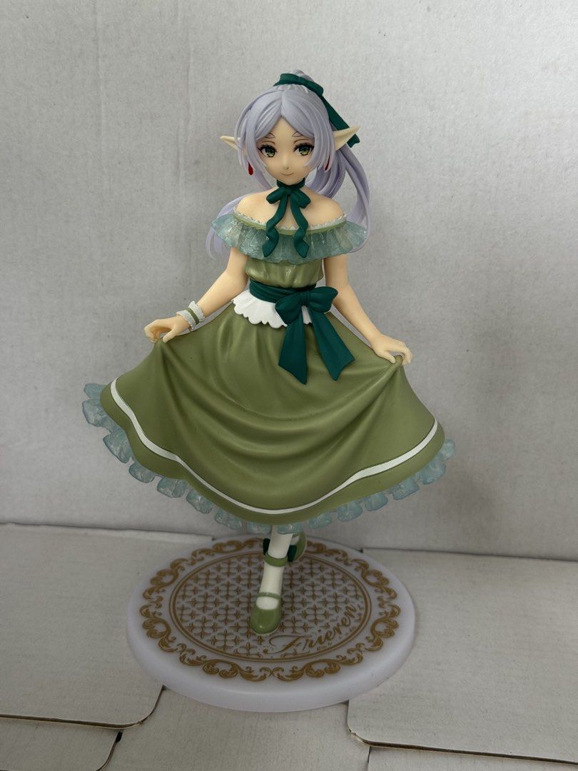 Frieren Figure Green Dress (Category: Figurines & Statues) located in President Roxas. Submitted by isserminator (Listing ID 1469955263, Image 1). Description: - Character: Frieren from the hit anime series - Outfit: Detailed green dress adorned with ruffles and bows - Appearance: Long grey-purple hair with a dark green ribbon, distinct elven ears, and green eyes - Base: White and gold decorative circular base featuring the official Frieren logo 