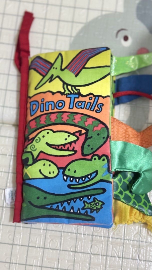 Galt Dino Tails Soft Activity Cloth Book (Category: Children's Books) located in Lucena. Submitted by jaejae___ (Listing ID 1470072240, Image 1). Description: - Brand: Galt (Dino Tails) - Type: Soft fabric interactive book for babies and toddlers - Features: Colourful dino illustrations, crinkly pages, and textured tails for sensory exploration - Bonus: Attached blue silicone teether for soothing gums - Condition: Clean, well-maintained, and read