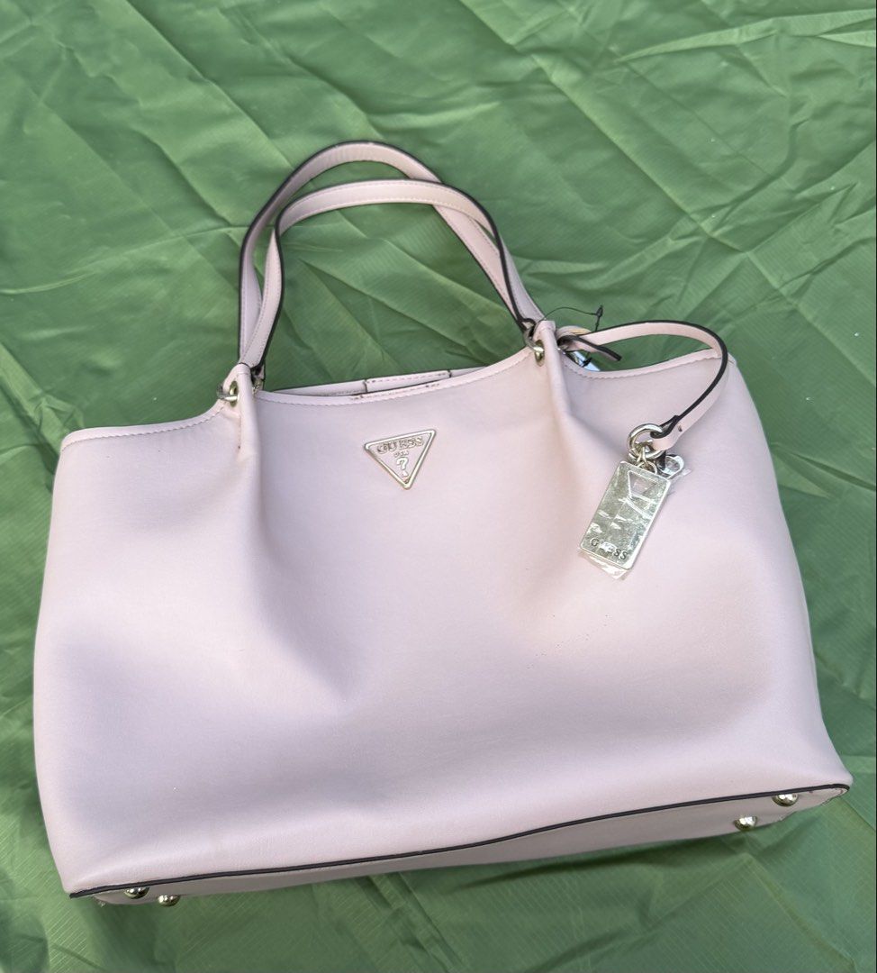 Guess Pink Tote Bag (Category: Shoulder Bags) located in Cavite. Submitted by maxs.bl (Listing ID 1469957348, Image 2). Description: - Brand: Guess - Style: Tote bag - Color: Light pink with luxury gold-tone hardware - Material: Premium faux leather - Features: Dual top handles, front metal logo plaque, protective bottom feet - Interior: Clean fabric lining, zipped center compartment, slip pockets - Closure: Secure magnetic snap - Condition: Well