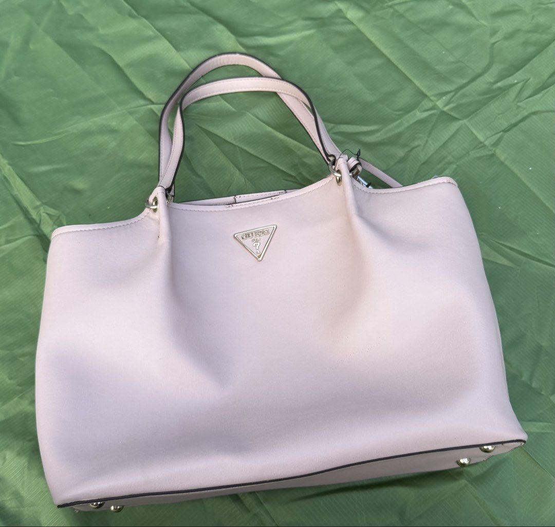 Guess Pink Tote Bag (Category: Shoulder Bags) located in Cavite. Submitted by maxs.bl (Listing ID 1469957348, Image 3). Description: - Brand: Guess - Style: Tote bag - Color: Light pink with luxury gold-tone hardware - Material: Premium faux leather - Features: Dual top handles, front metal logo plaque, protective bottom feet - Interior: Clean fabric lining, zipped center compartment, slip pockets - Closure: Secure magnetic snap - Condition: Well