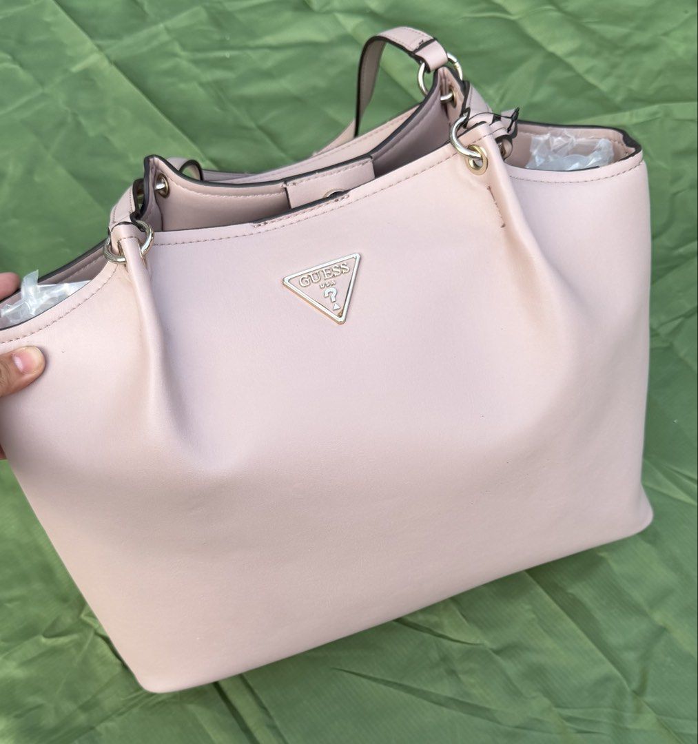 Guess Pink Tote Bag (Category: Shoulder Bags) located in Cavite. Submitted by maxs.bl (Listing ID 1469957348, Image 1). Description: - Brand: Guess - Style: Tote bag - Color: Light pink with luxury gold-tone hardware - Material: Premium faux leather - Features: Dual top handles, front metal logo plaque, protective bottom feet - Interior: Clean fabric lining, zipped center compartment, slip pockets - Closure: Secure magnetic snap - Condition: Well