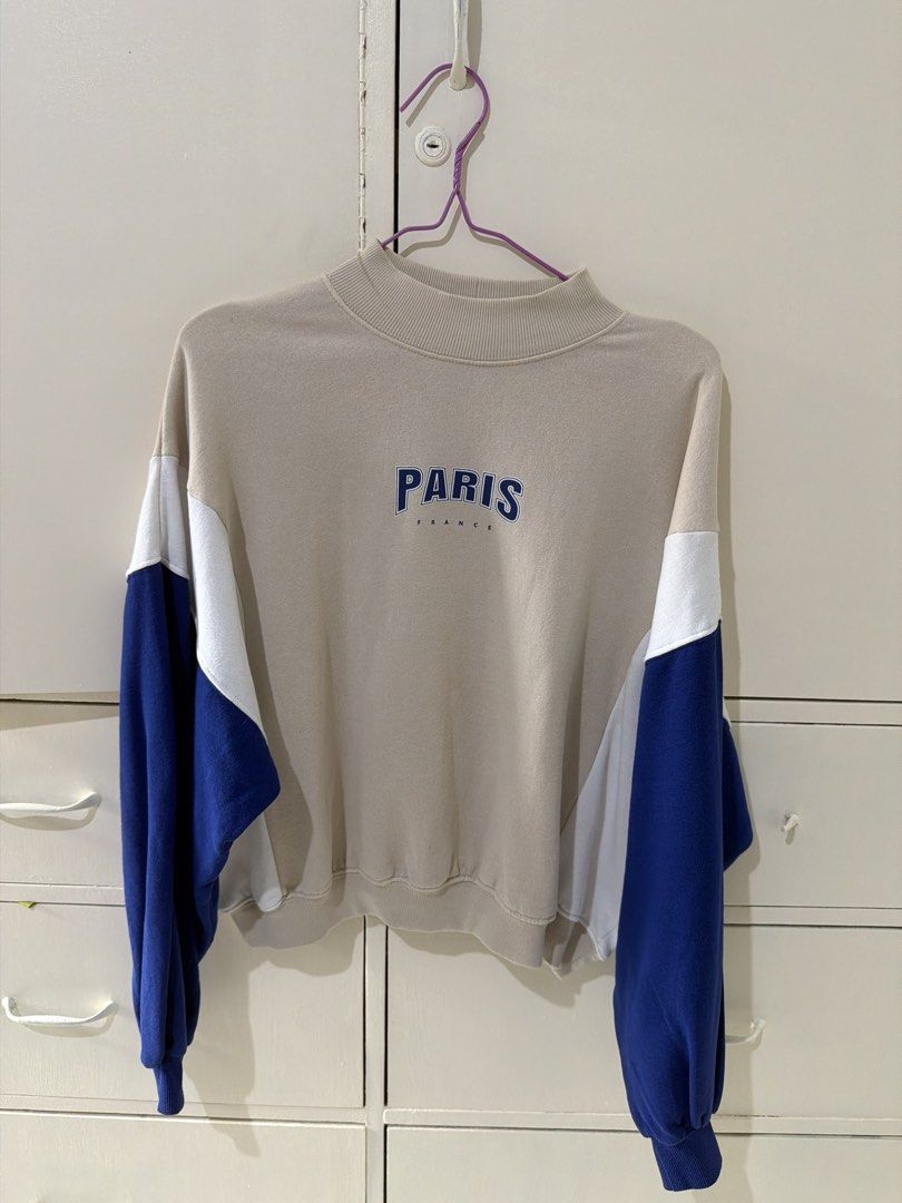 H&M Divided Paris Colorblock Sweatshirt Size M (Category: Longsleeves) located in Rizal. Submitted by kyliemaine (Listing ID 1470014504, Image 1). Description: - Brand/Model: H&M Divided Colorblock Sweatshirt - Colorway: Beige, white, and blue - Design: Bold 'PARIS FRANCE' lettering on the chest - Fit: Relaxed, oversized fit with drop shoulders - Details: Mock neck collar, ribbed cuffs and hem - Interior: Soft fleece lining for extra warmth - Siz