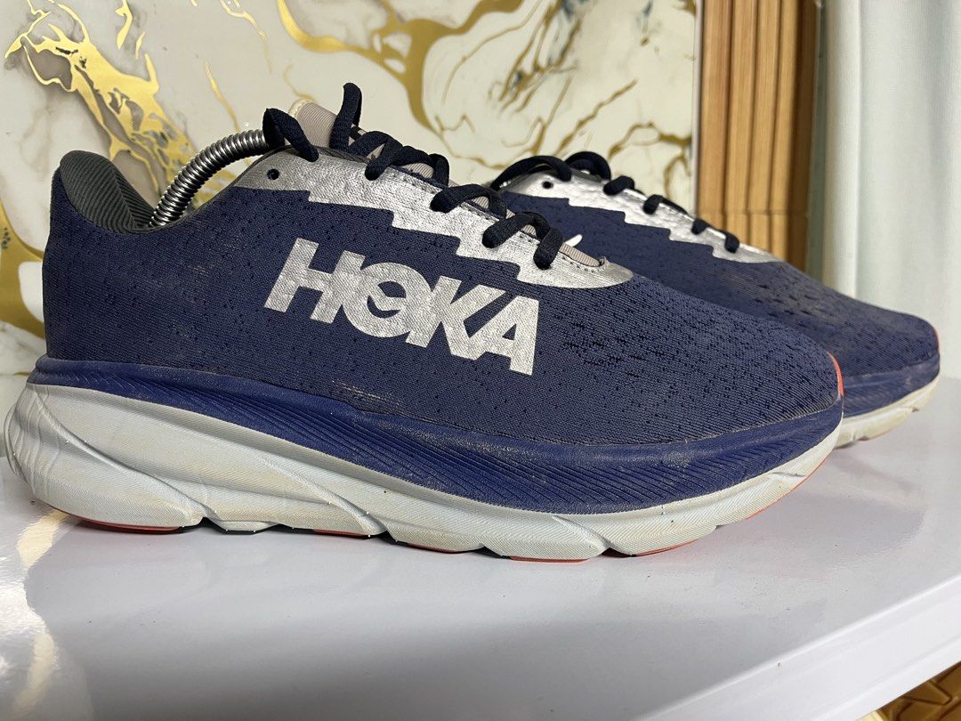 Hoka One One Running Shoes Blue Silver (Category: Sneakers) located in Manila. Submitted by lkiss13 (Listing ID 1470074385, Image 1). Description: - Brand: Hoka - Color: Navy blue with large silver branding and metallic silver panels - Cushioning: Thick white and blue cushioned midsole - Outsole: Orange and white rubber with moderate tread wear - Condition: Uppers show slight dirt marks from previous runs - Usage: Great daily trainers with plenty
