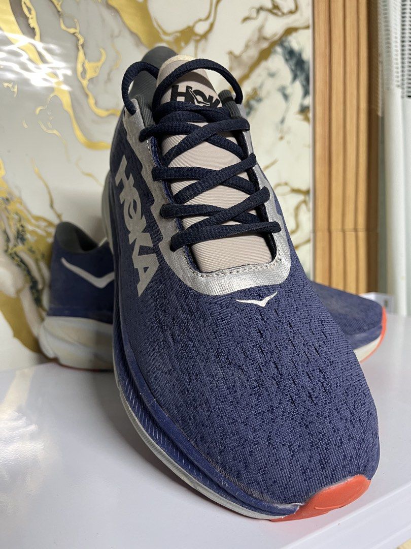Hoka One One Running Shoes Blue Silver (Category: Sneakers) located in Manila. Submitted by lkiss13 (Listing ID 1470074385, Image 2). Description: - Brand: Hoka - Color: Navy blue with large silver branding and metallic silver panels - Cushioning: Thick white and blue cushioned midsole - Outsole: Orange and white rubber with moderate tread wear - Condition: Uppers show slight dirt marks from previous runs - Usage: Great daily trainers with plenty