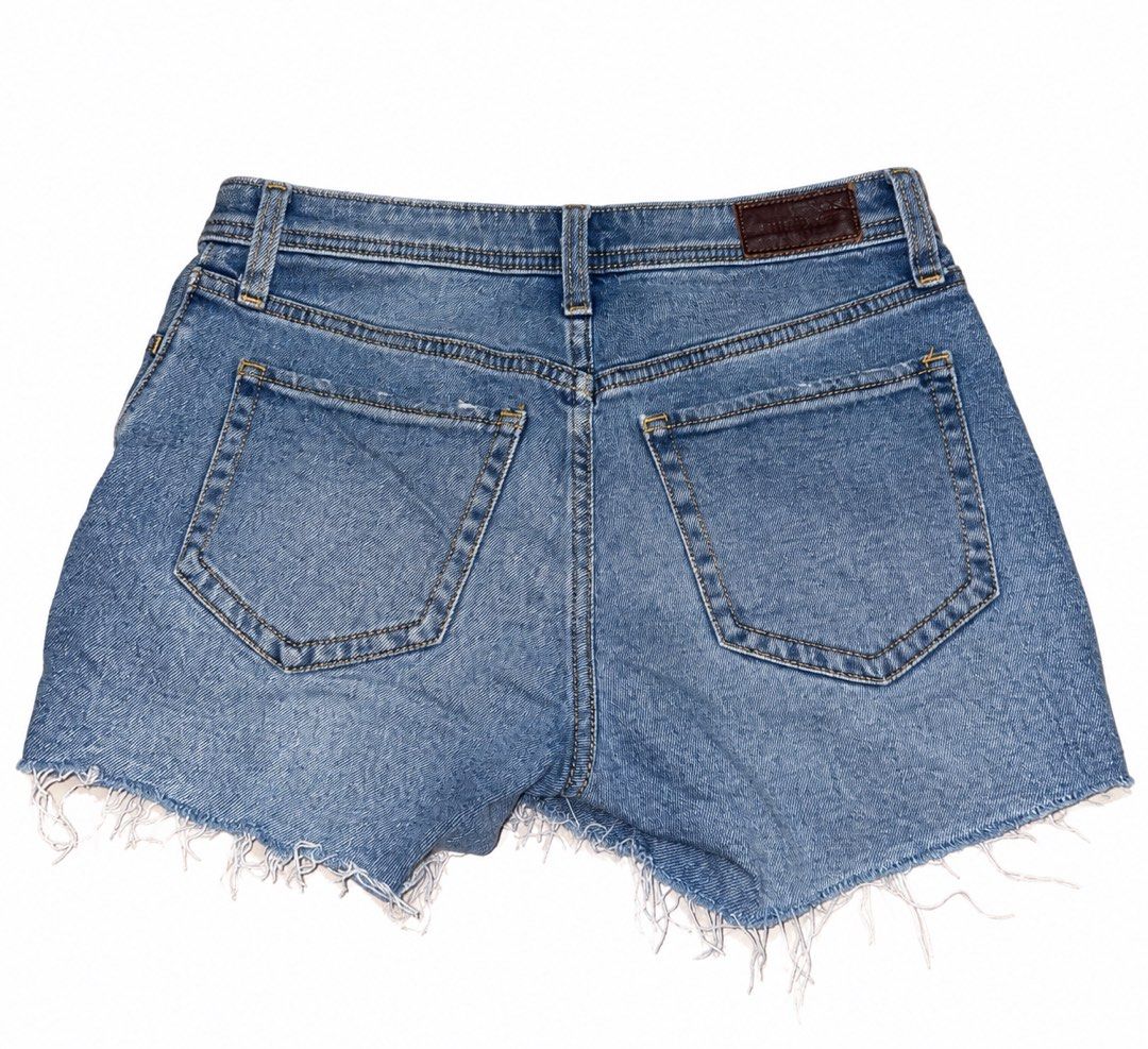 Hollister Shorts (Category: Shorts) located in Marikina City. Submitted by ziaziaaa (Listing ID 1470084846, Image 2). Description: - Color/Wash: Medium blue denim - Closure: Button fly with copper-tone metal hardware - Details: Raw frayed hem, distressed patch on right thigh, brown leather brand patch on back waistband - Pockets: Two front pockets, one coin pocket, two back patch pockets - Style: Classic cut-off shorts, ideal for warm weather.