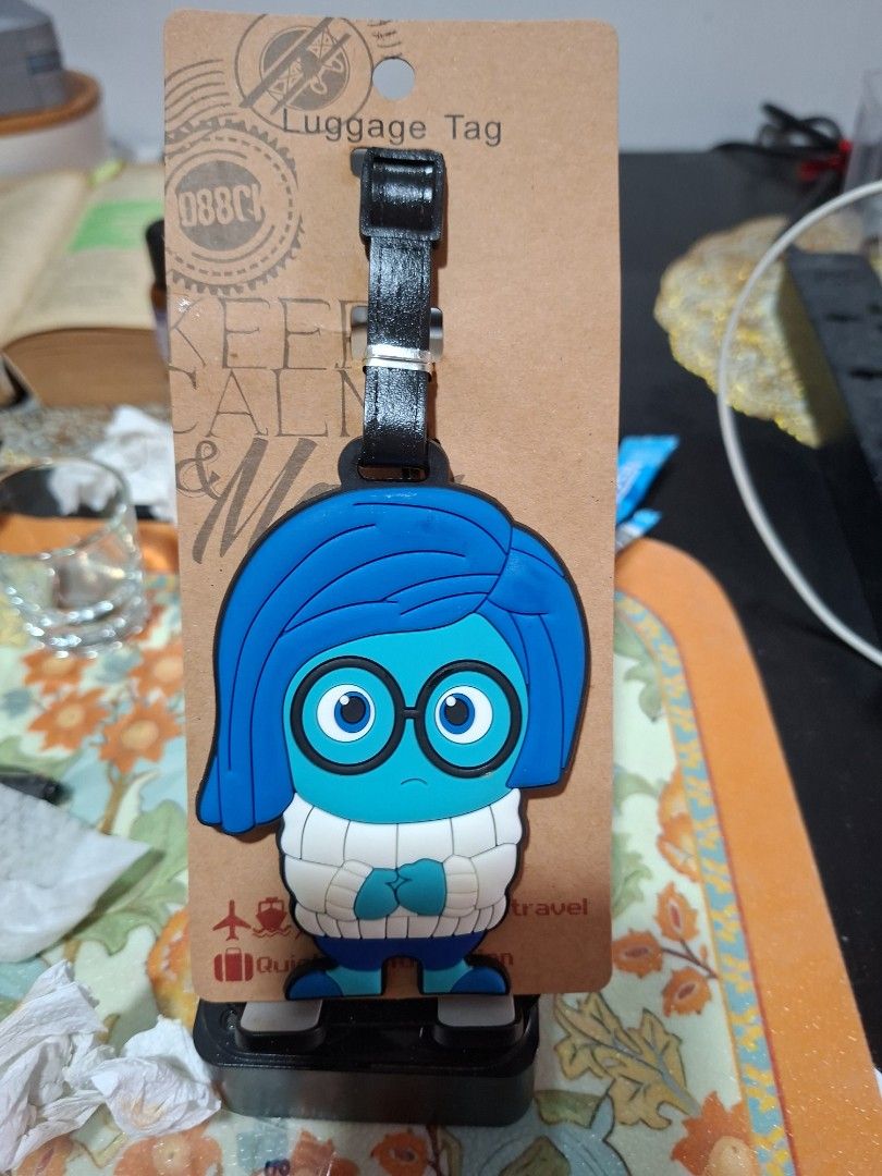 Inside Out Sadness Silicone Luggage Tag (Category: Luggage) located in Bulacan. Submitted by rafaesarisari (Listing ID 1469991895, Image 2). Description: - Character: Sadness from Disney Pixar's Inside Out - Material: High-quality molded silicone - Design: Bright blue hair, glasses, and white sweater - Attachment: Secure black strap with a buckle fastener - Condition: Brand new, sealed in original packaging - Ideal for: Luggage, backpacks, and Di