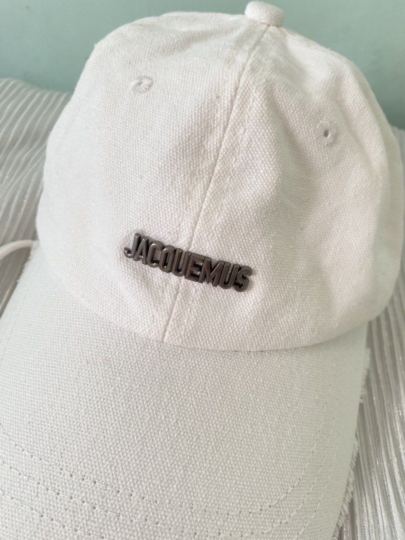Jacquemus White Cotton Baseball Cap (Category: Caps & Hats) located in Tabaco. Submitted by camila_p (Listing ID 1470048626, Image 3). Description: - Authentic Jacquemus baseball cap in crisp white cotton canvas - Features a sleek metal JACQUEMUS lettering logo on the front - Trendy raw frayed edge detailing on the brim - Adjustable back strap with a branded silver-tone metal buckle - Interior includes official black and white brand tags (Made in