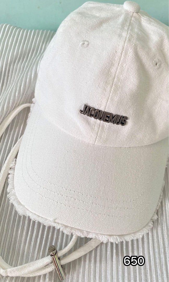Jacquemus White Cotton Baseball Cap (Category: Caps & Hats) located in Tabaco. Submitted by camila_p (Listing ID 1470048626, Image 1). Description: - Authentic Jacquemus baseball cap in crisp white cotton canvas - Features a sleek metal JACQUEMUS lettering logo on the front - Trendy raw frayed edge detailing on the brim - Adjustable back strap with a branded silver-tone metal buckle - Interior includes official black and white brand tags (Made in