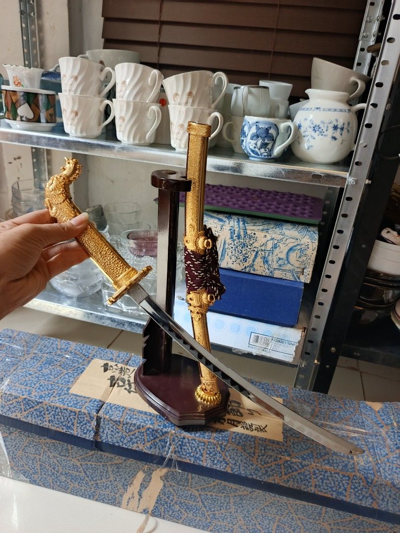 Japanese Samurai Sword and Bow Decorative Set with Stands (Category: Vintage Collectibles) located in Quezon City. Submitted by valerieluarez (Listing ID 1470132360, Image 1). Description: - Japanese ornamental decor set (Golden katana replica + mini bow & arrow) - Detailed dragon handle and ornate gold scabbard with purple/white wrapping - Includes feathered arrows - Comes with dark wood display stands for both items - Great statement pieces for