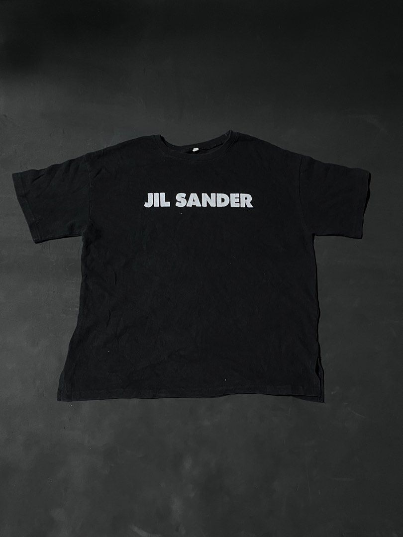 Jil Sander Black Logo T-Shirt (Category: Shirts) located in Andop. Submitted by outclickz_00 (Listing ID 1470123418, Image 1). Description: - Brand: Jil Sander 22/25 - Color: Black with contrasting white logo - Material: Premium cotton - Fit: Relaxed streetwear fit with classic short sleeves - Features: Chest logo print and trendy side slit hem details - Condition: Brand new / Excellent quality - Perfect everyday basic piece for a minimalist look