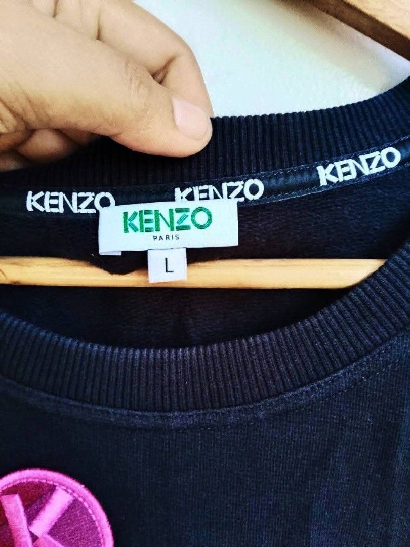 Kenzo Paris Black Sweatshirt Patch Design Size L (Category: Coats, Jackets and Outerwear) located in Bogo. Submitted by algarme2018 (Listing ID 1470054498, Image 2). Description: - Brand: Kenzo Paris - Size: Large - Dimes: W21 * L25 - Color: Black - Material: Comfortable cotton blend - Origin: Made in Portugal - Design: Graphic patches (palm tree, glacier, pink 'K' logo) with bold 'KENZO' chest lettering - Details: Ribbed collar, cuffs, and hem w