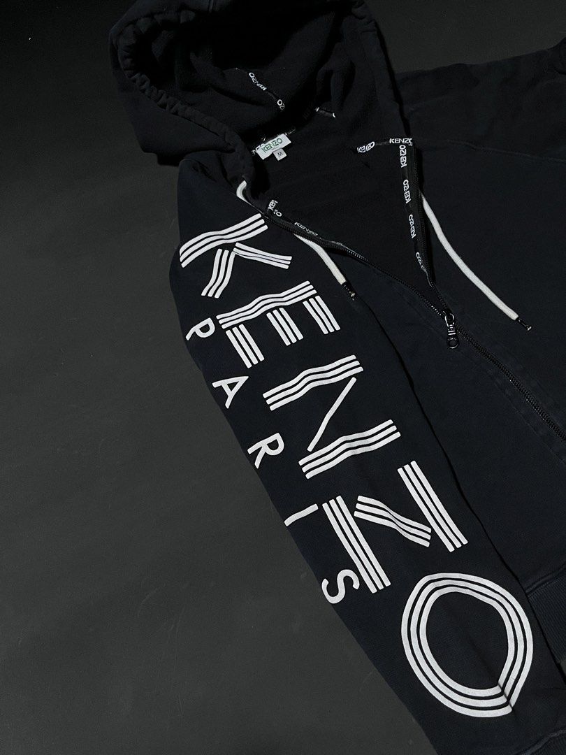 Kenzo Paris Black Zip-Up Hoodie (Category: Coats, Jackets and Outerwear) located in Andop. Submitted by outclickz_00 (Listing ID 1470120568, Image 2). Description: - Brand: Kenzo Paris - Style: Zip-up hoodie - Color: Black with bold white logo graphics on the right sleeve - Size: Medium 20/25 - Features: Drawstring hood with branded tape details, full front zipper, ribbed cuffs and hem, and two front pockets - Condition: Excellent, interior tags 