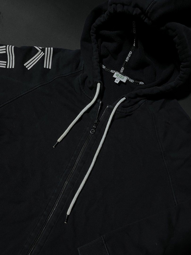 Kenzo Paris Black Zip-Up Hoodie (Category: Coats, Jackets and Outerwear) located in Andop. Submitted by outclickz_00 (Listing ID 1470120568, Image 3). Description: - Brand: Kenzo Paris - Style: Zip-up hoodie - Color: Black with bold white logo graphics on the right sleeve - Size: Medium 20/25 - Features: Drawstring hood with branded tape details, full front zipper, ribbed cuffs and hem, and two front pockets - Condition: Excellent, interior tags 