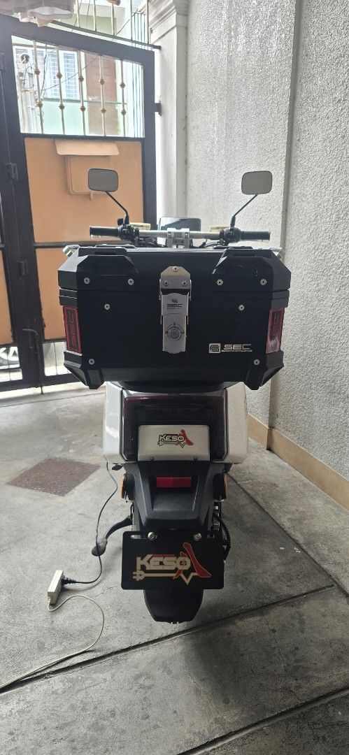 Keso Electric Scooter with SEC Top Box (Category: Motorbikes for Sale) located in Manila. Submitted by dabbyd (Listing ID 1470076710, Image 3). Description: White electric scooter, Keso branding. Equipped with SEC top box on the rear rack. Modern LED headlights, turn signals on handlebars, and side mirrors attached. Dual standing kickstand deployed. Charger plugged in on the floorboard area. Ready for city commutes. RFS : seldom used.. 172km odo 