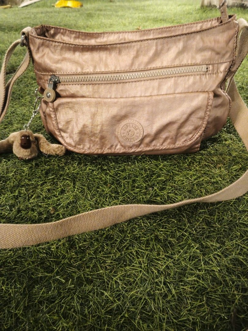 Kipling Rose Gold Nylon Crossbody Bag (Category: Cross-body Bags) located in Lucena. Submitted by jmjm31 (Listing ID 1470082376, Image 1). Description: - Brand: Kipling - Color: Rose Gold - Material: Durable Nylon - Condition: Brand new with tags tucked in pocket, clean interior lining - Features: Multiple exterior zip compartments, spacious main interior with slip pockets - Extras: Secure key leash and signature furry monkey keychain - Strap: Lo