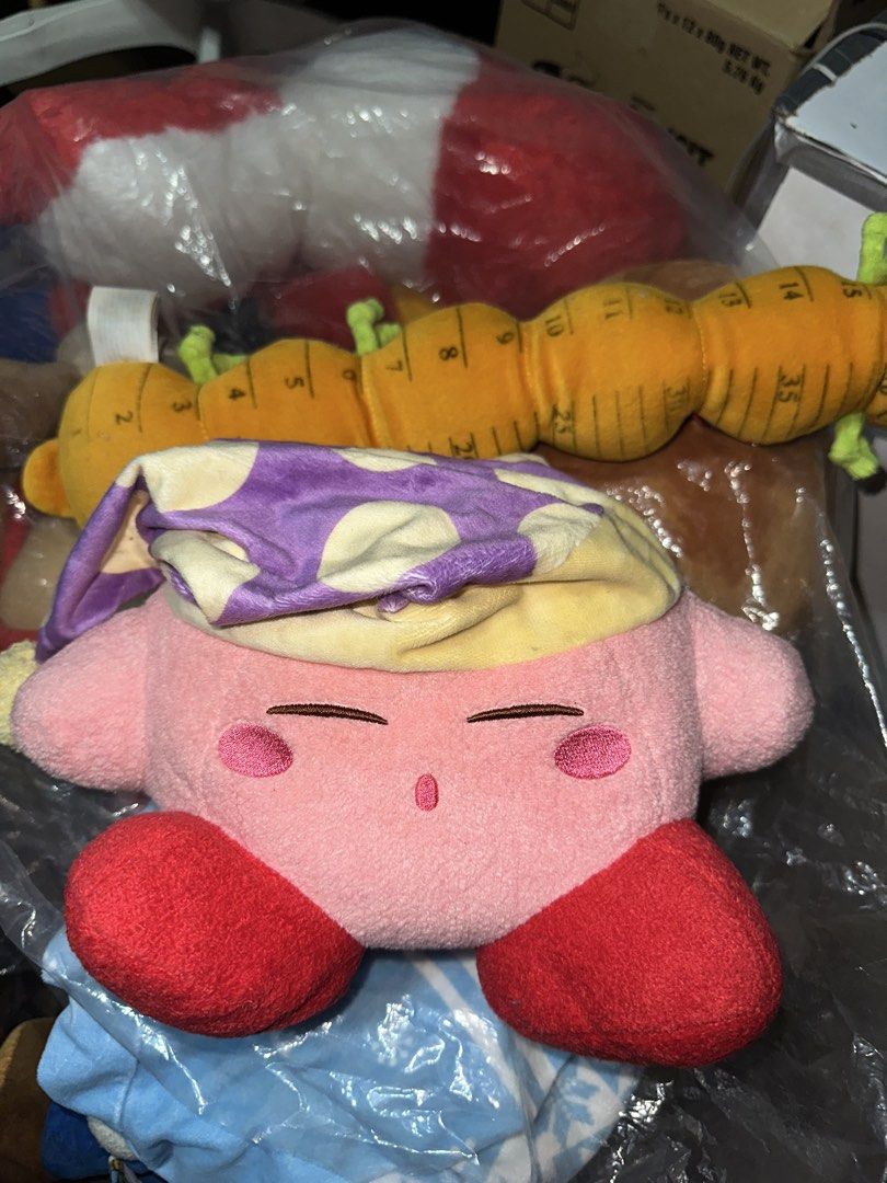 Kirby with Sleeping Cap with papertag (Category: Plushies & Soft Toys) located in Pasig City. Submitted by katplush_superlove (Listing ID 1470043021, Image 1). Description: - Official-style cute Kirby plush figure in a sleeping pose - Features a cozy purple and yellow patterned sleeping cap with a pom-pom - Made with ultra-soft, huggable pink fabric with embroidered closed eyes and red feet - Tag attached near the side, great for collectors - Per