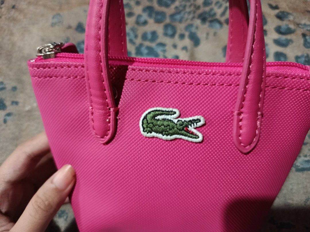 Lacoste Hot Pink Mini Tote Pouch Bag (Category: Purses & Pouches) located in Manila. Submitted by purewolf.c917d2 (Listing ID 1469956947, Image 2). Description: Hot pink Lacoste mini tote pouch. Textured canvas material with dual top handles. Zipper closure featuring a matching pink pull tab embossed with Lacoste branding. Classic green crocodile logo embroidered on the front. Compact size, great for carrying small essentials in your main bag or 