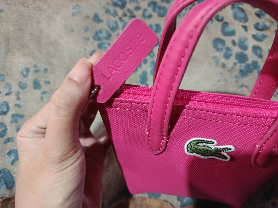 Lacoste Hot Pink Mini Tote Pouch Bag (Category: Purses & Pouches) located in Manila. Submitted by purewolf.c917d2 (Listing ID 1469956947, Image 3). Description: Hot pink Lacoste mini tote pouch. Textured canvas material with dual top handles. Zipper closure featuring a matching pink pull tab embossed with Lacoste branding. Classic green crocodile logo embroidered on the front. Compact size, great for carrying small essentials in your main bag or 