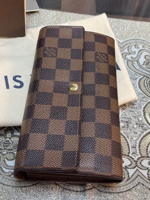 Louis Vuitton Damier Sarah Wallet (Category: Luxury Bags & Wallets) located in Pasay City. Submitted by watch.authentic_ph (Listing ID 1470007643, Image 3). Description: - Brand: Louis Vuitton - Pattern: Classic Damier Ebene canvas (Brown check) - Closure: Front flap with snap button - Interior: Multiple compartments for cards and cash - Condition: Well-maintained shape with clean edges - Inclusions: Original dust bag and branded box included.