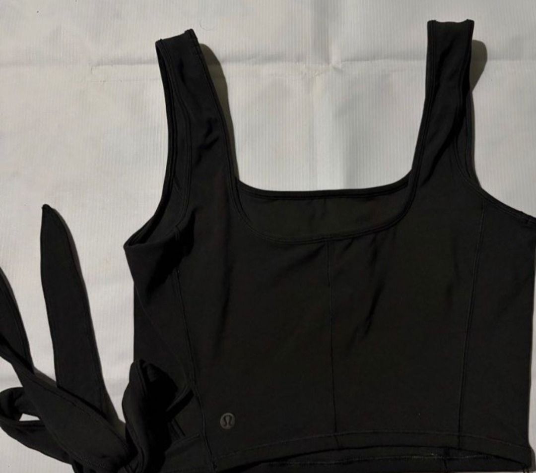 Lululemon Black Tie-Side Tank Top Crop Top (Category: Sleeveless) located in Pasig City. Submitted by peachesncreams (Listing ID 1470102600, Image 3). Description: - Brand: Lululemon - Style: Black cropped tank top with square neckline and wide straps - Features: Adjustable side tie wrap fit, racerback, and reflective logo near the hem - Material: Soft, stretchy athletic fabric - Condition: Excellent/Good as new - Best for: Workouts, running erra