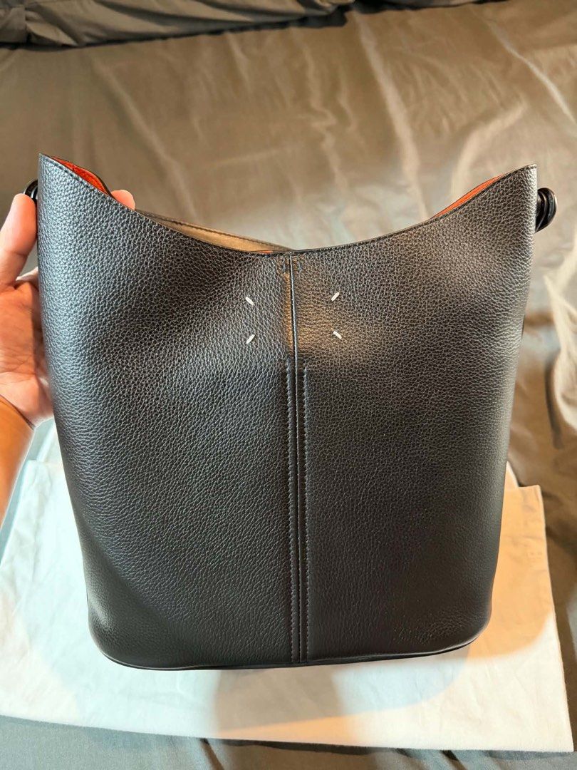 Maison Margiela Black Leather Bucket Bag (Category: Luxury Bags & Wallets) located in Manila. Submitted by dalandansoy (Listing ID 1469974974, Image 2). Description: - Brand: Maison Margiela - Style: Bucket bag in black grained leather - Interior: Contrast vibrant orange - Details: Iconic four white stitches on front - Strap: Adjustable shoulder strap included - Inclusion: Dust bag - Condition: Clean structure with minimal wear overall.