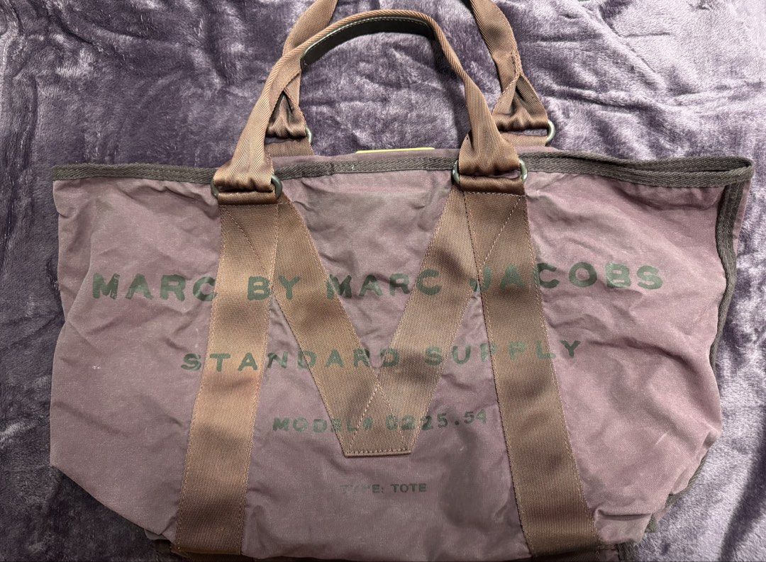 Marc by Marc Jacobs Standard Supply Tote Bag (Category: Tote Bags) located in Valenzuela. Submitted by sofiasticated.decluttering (Listing ID 1470081100, Image 1). Description: - Brand: Marc by Marc Jacobs (Model M00225.54) - Color: Purple canvas with brown webbed straps and handles - Features: Signature leather patch inside and outside, secure velcro top closure - Capacity: Spacious main compartment perfect for daily essentials - Style: Classic 