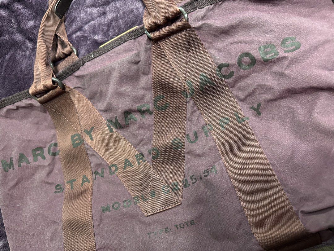 Marc by Marc Jacobs Standard Supply Tote Bag (Category: Tote Bags) located in Valenzuela. Submitted by sofiasticated.decluttering (Listing ID 1470081100, Image 3). Description: - Brand: Marc by Marc Jacobs (Model M00225.54) - Color: Purple canvas with brown webbed straps and handles - Features: Signature leather patch inside and outside, secure velcro top closure - Capacity: Spacious main compartment perfect for daily essentials - Style: Classic 