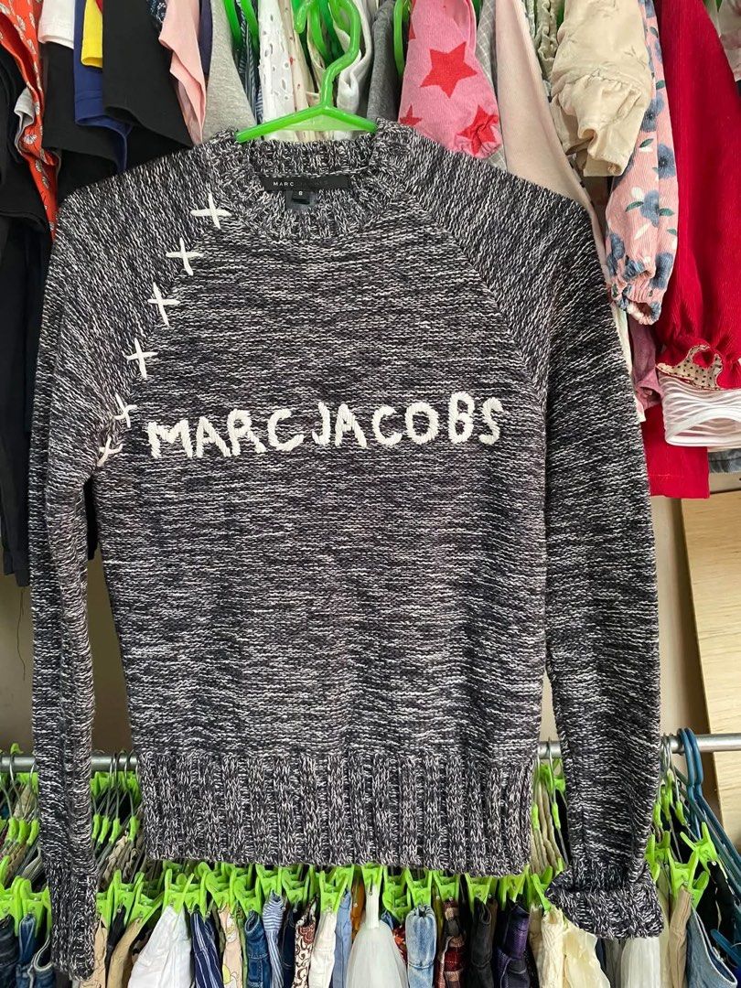Marc Jacobs Black White Knit Sweater Size S (Category: Longsleeves) located in Tabuk. Submitted by collectors_thrift_shop (Listing ID 1470047491, Image 1). Description: - Brand: Marc Jacobs - Size: S (tag attached inside collar) - Color/Pattern: Black and white heathered yarn - Design: White embroidered lettering across the chest with decorative white stitching on the right shoulder seam - Details: Ribbed cuffs and hem - Care: Dry clean only - Co