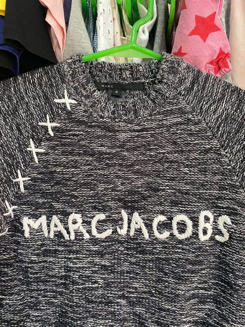 Marc Jacobs Black White Knit Sweater Size S (Category: Longsleeves) located in Tabuk. Submitted by collectors_thrift_shop (Listing ID 1470047491, Image 2). Description: - Brand: Marc Jacobs - Size: S (tag attached inside collar) - Color/Pattern: Black and white heathered yarn - Design: White embroidered lettering across the chest with decorative white stitching on the right shoulder seam - Details: Ribbed cuffs and hem - Care: Dry clean only - Co