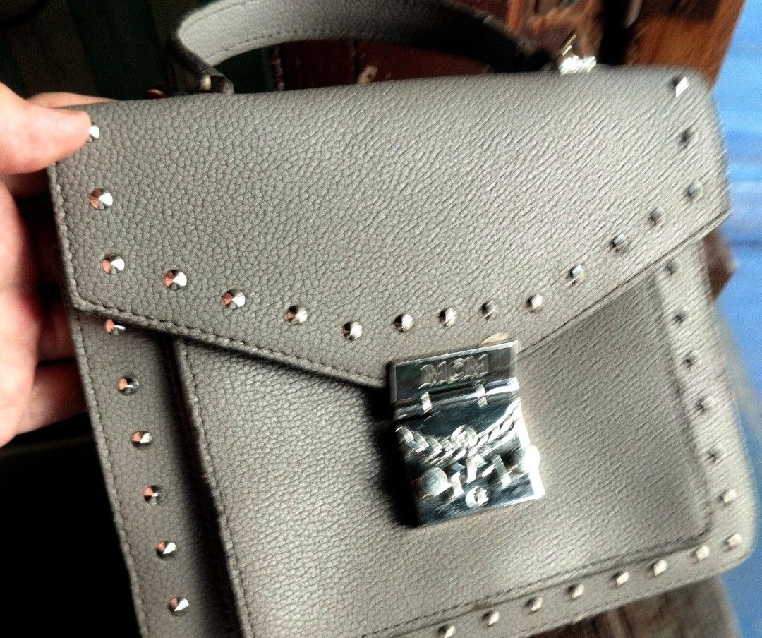 MCM Grey Leather Studded Satchel Handbag (Category: Cross-body Bags) located in Manila. Submitted by lene48 (Listing ID 1470088882, Image 1). Description: - Material: Grey pebbled leather exterior with stylish metal studs - Hardware: Secure silver-tone front lock closure - Interior: Vibrant bright orange lining featuring a zippered pocket and brand logo plaque - Design: Elegant top handle styleflaw sa rubber lining n replace sling. .