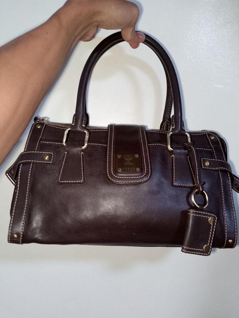 MCM Muchen Dark Brown Leather Handbag (Category: Luxury Bags & Wallets) located in Manila. Submitted by mjthrifted_second (Listing ID 1469981432, Image 1). Description: - Brand: MCM München - Color: Rich dark brown with contrast white stitching - Material: Premium structured leather - Hardware: Brass-tone with side buckle accents - Closure: Zip-top secure closure - Exterior: Front flap pocket with metal logo plaque (Model X3330) and hanging charm