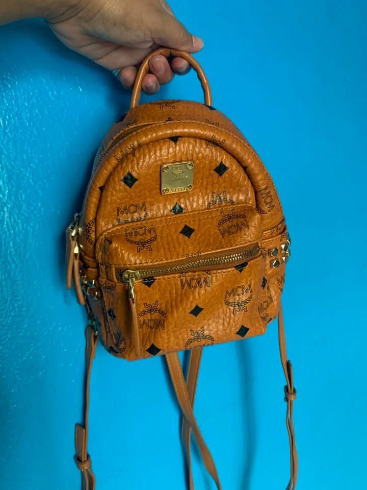 MCM Stark Visetos Mini Backpack Cognac (Category: Luxury Bags & Wallets) located in Batangas. Submitted by bling_bling_and_more_by_dulce (Listing ID 1470038104, Image 1). Description: 800 each - MCM mini backpack in the signature classic cognac colorway - Iconic all-over print with black diamonds and MCM logos - Front zip pocket accented with edgy side stud details - Secure top handle and comfortable, adjustable leather shoulder straps - Luxuriou