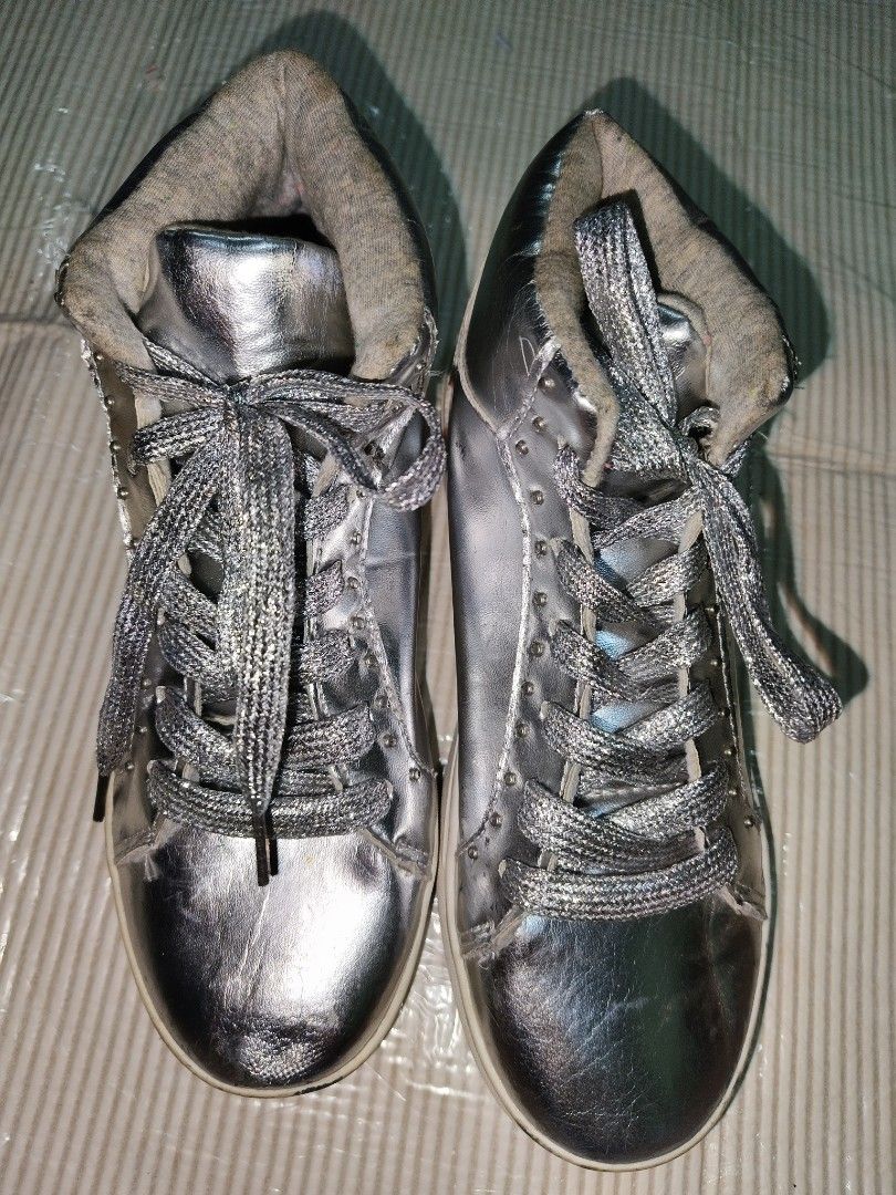 Metallic silver high-top sneakers with laces (Category: Sneakers) located in Manila. Submitted by reascheyss51406 (Listing ID 1469974107, Image 3). Description: - Style: Silver metallic high-top sneakers with a shiny finish - Accents: Glitter laces, side studs, and cozy warm lining around the ankle collar - Soles: Classic white rubber soles - Condition: Minor visible wear on the toe box and light creases on the upper material - Perfect for adding