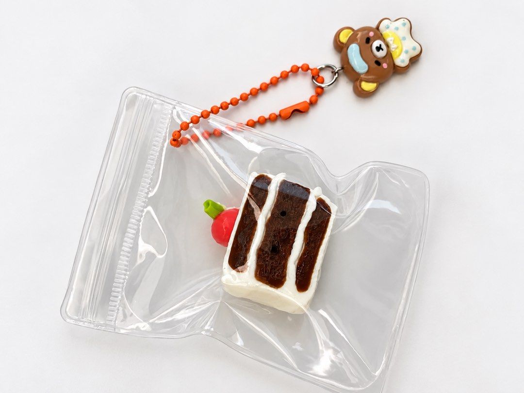 Mini Cute chocolate cake keychain with bear charm (Category: Plushies & Soft Toys) located in Manila. Submitted by nagets1001 (Listing ID 1470054652, Image 1). Description: - Adorable chocolate cake slice charm with white frosting and a red cherry - Includes a cute brown bear character wearing a chef hat and an orange ball chain - Brand new, still sealed inside its original clear plastic ziplock packaging - Fun and collectible accessory straight 