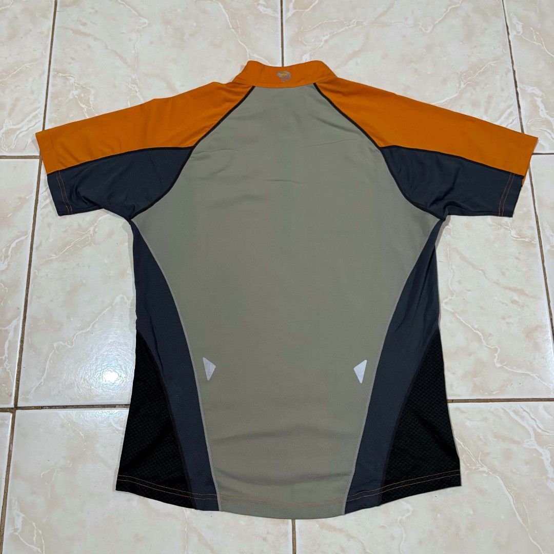 Mountain Hardwear Orange (Category: Activewear) located in El Salvador. Submitted by pretiezt2001 (Listing ID 1470047317, Image 2). Description: - Brand: Mountain Hardwear - Color: Bright orange and dark grey - Design: Short sleeves, half-zip front, and high collar - Breathability: Mesh fabric panels on shoulders and back yoke - Safety: Reflective piping details along seams - Branding: Clear logo printed on the chest - Ideal for: Outdoor rides, r