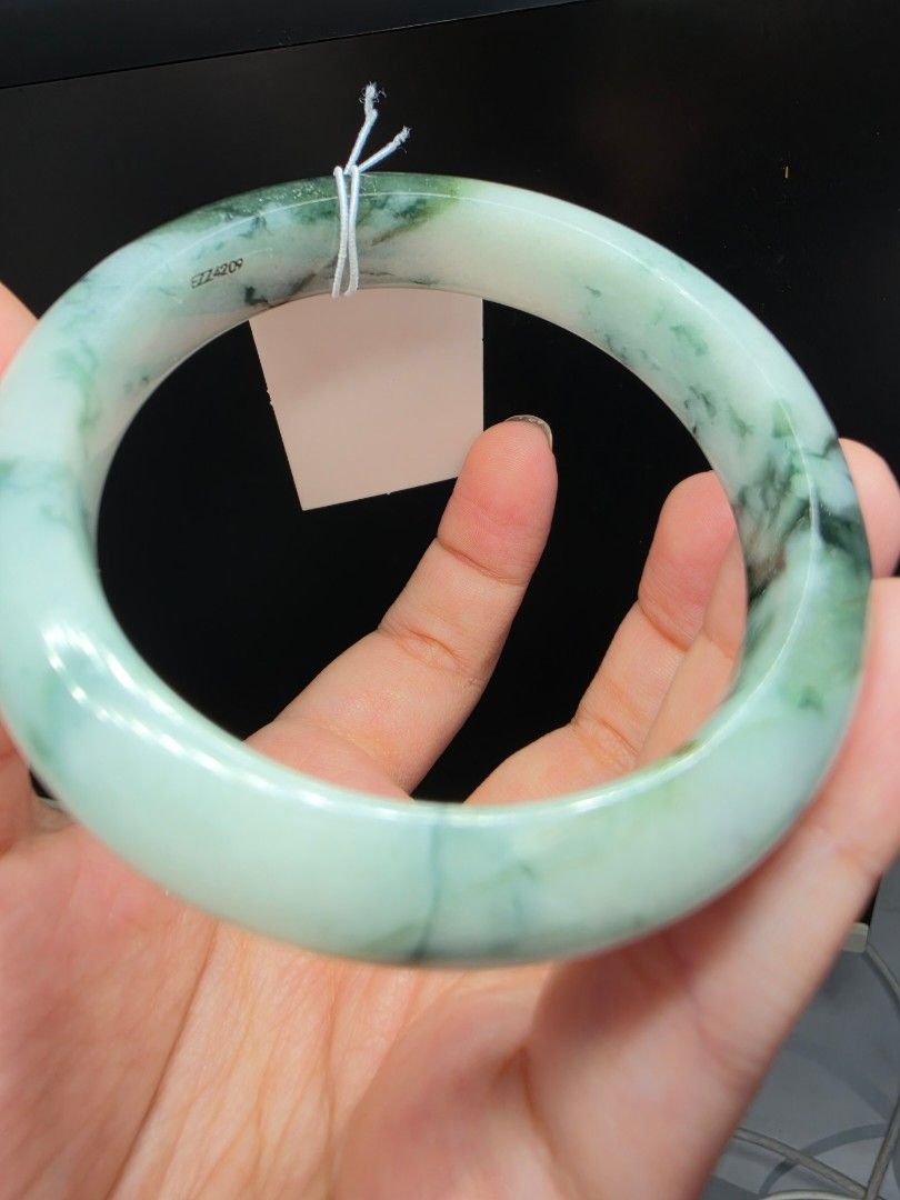 Natural Spicy Green Jadeite Bangle Bracelet with floating Pattern 58.9mm (Category: Bracelets) located in Manila. Submitted by jadeitesph (Listing ID 1470139996, Image 1). Description: - Material: Genuine solid green jadeite stone -58.9 - Design: Traditional round shape with a smooth, fully polished surface - Appearance: Beautiful mix of dark green patches and mottled white areas - Authenticity details: Attached paper tag and small engraved seria