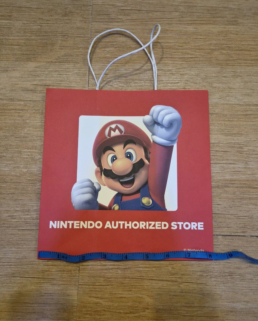 Nintendo Authorized Store Mario Paper Gift Bag (Category: Character Goods) located in Manila. Submitted by golden_brain (Listing ID 1470116536, Image 2). Description: - Official merchandise from the Nintendo Authorized Store - Features an iconic Mario graphic on the front and Nintendo Switch logo on the back - Sturdy white rope handles attached at the top - Dimensions are ideal for collecting convention merch or wrapping special gifts for gamers.