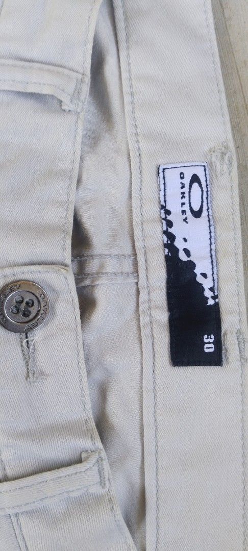 Oakley Cargo Pants Cream Size 30 (Category: Jeans) located in Manila. Submitted by 27moby (Listing ID 1470005912, Image 3). Description: - Brand/Model: Oakley Cargo Pants - Color: Cream - Size: Waist 30 - Material: Cotton-poly blend with stretch - Fit: Straight leg with front panel seam details - Pockets: Multiple utility pockets with button closures and back welt pockets with flap covers - Details: Distinctive orange Oakley embroidery on the rig